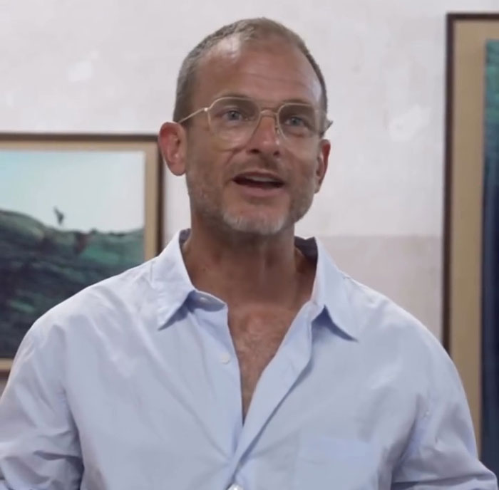 Man wearing glasses and a light blue shirt speaking indoors, related to VF photographer defending Karoline Leavitt close-up. Man wearing glasses and a light blue shirt speaking indoors, related to VF photographer defending Karoline Leavitt close-up.