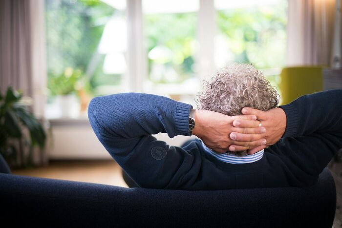 A person relaxing on a couch with hands behind head, reflecting on harmless but toxic habits in a bright room.