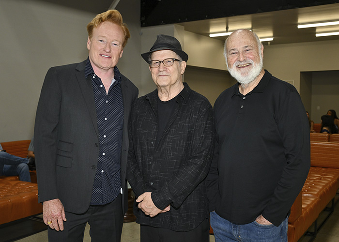 Conan O’Brien with two men at an event, posing for a photo in a room with leather seating and industrial lighting. Conan O’Brien with two men at an event, posing for a photo in a room with leather seating and industrial lighting.