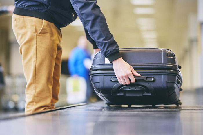 Person handling black suitcase on airport baggage carousel illustrating luggage policy dispute and airline worker emotions.