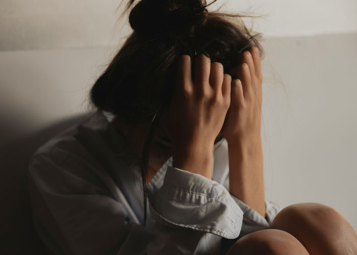 Stressed woman holding head in hands in dim light, reflecting tension related to closet door argument and public clap back. Stressed woman holding head in hands in dim light, reflecting tension related to closet door argument and public clap back.