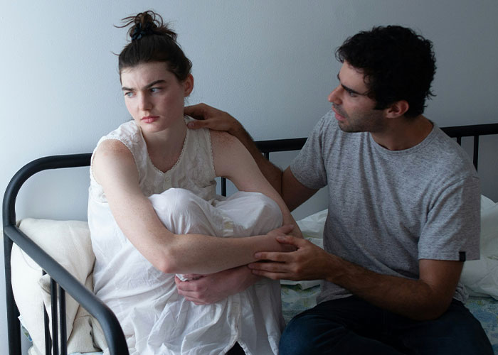 Couple in tense conversation on bed, woman upset and avoiding eye contact, man trying to comfort her after argument. Couple in tense conversation on bed, woman upset and avoiding eye contact, man trying to comfort her after argument.