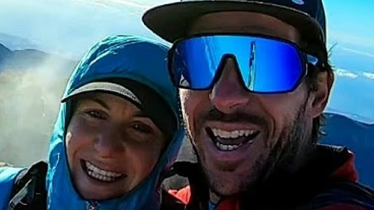 Couple wearing outdoor gear smiling during a mountain hike, related to woman abandoned on Austriau2019s highest peak.
