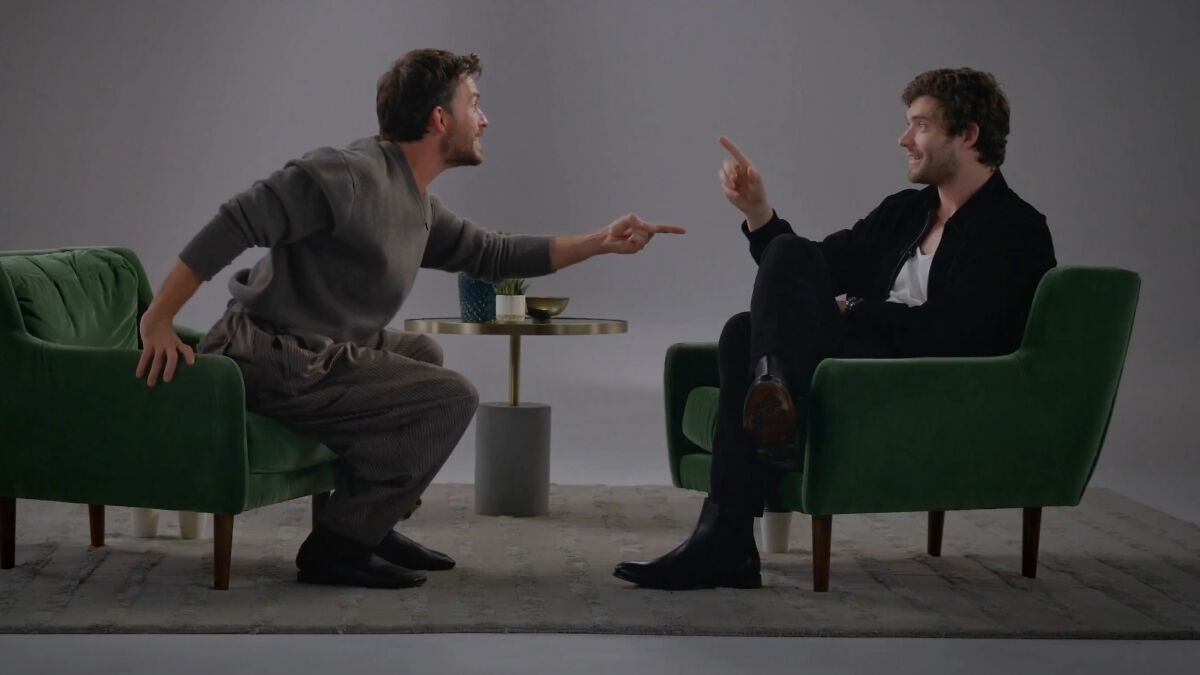 David Corenswet and Jonathan Bailey seated in green chairs, engaging in a lively discussion about masculinity perspectives.