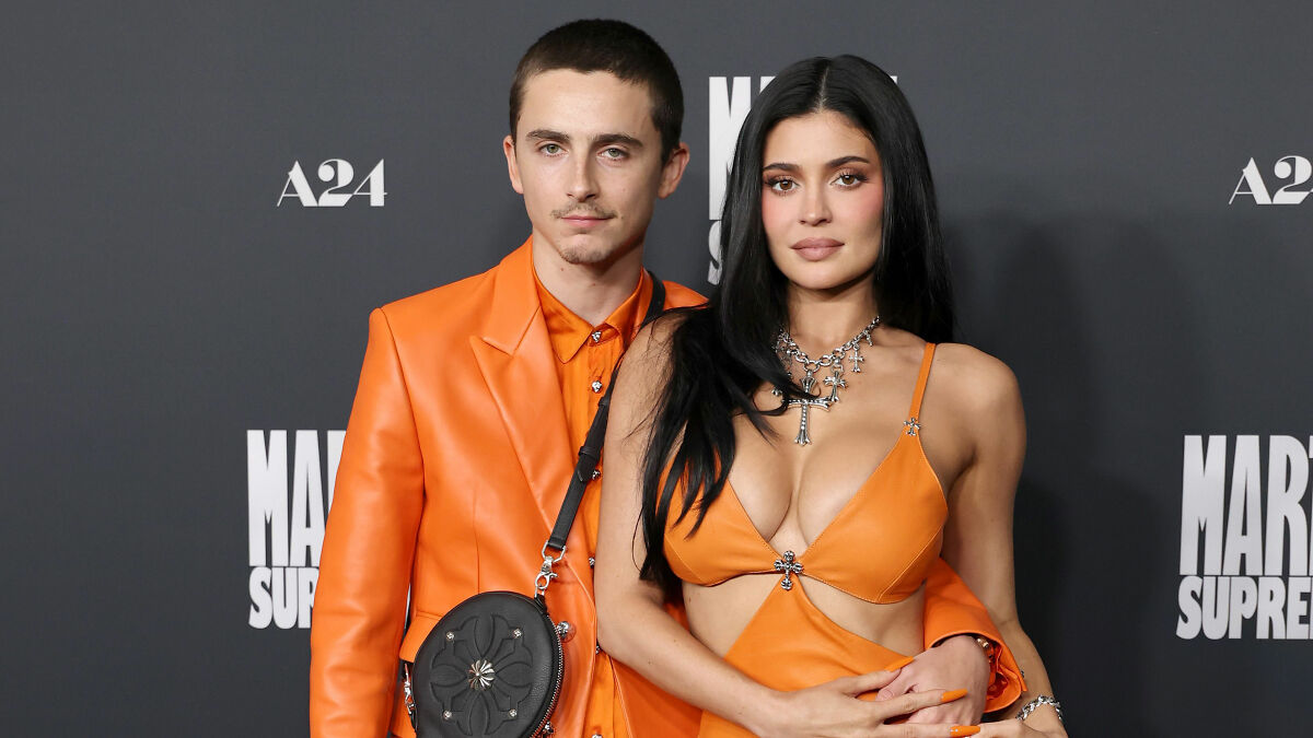 Timothu00e9e Chalamet and Kylie Jenner in coordinated orange outfits posing together on the red carpet at a movie premiere.