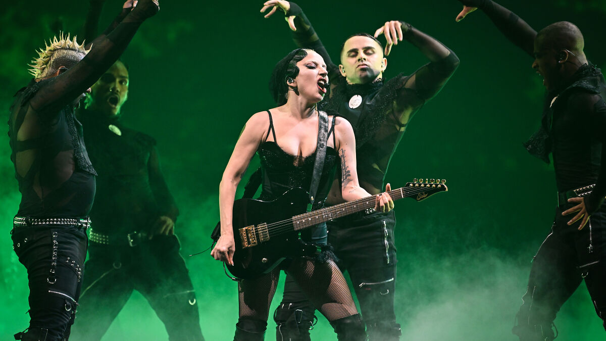 Lady Gaga performing on stage with dancers in a dramatic green-lit concert setting.