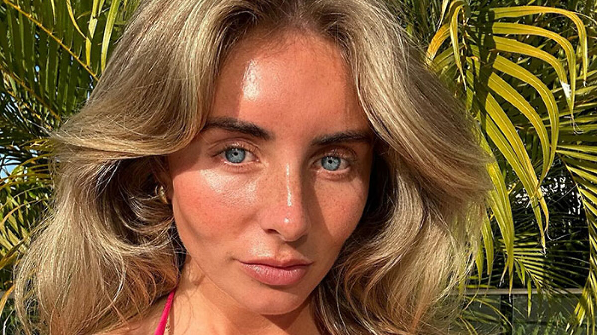 Close-up of a woman with blonde hair and blue eyes outdoors near green palm leaves, related to snitch who reported Bonnie Blue.