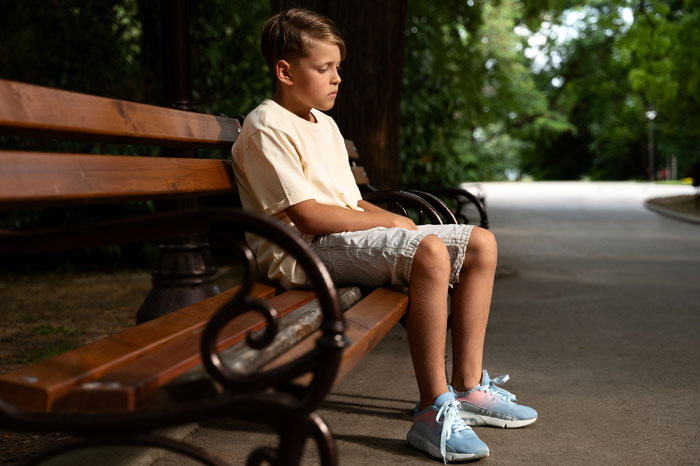 Sad young boy sitting alone on a park bench, reflecting the impact of CPS intervention and childhood distress.