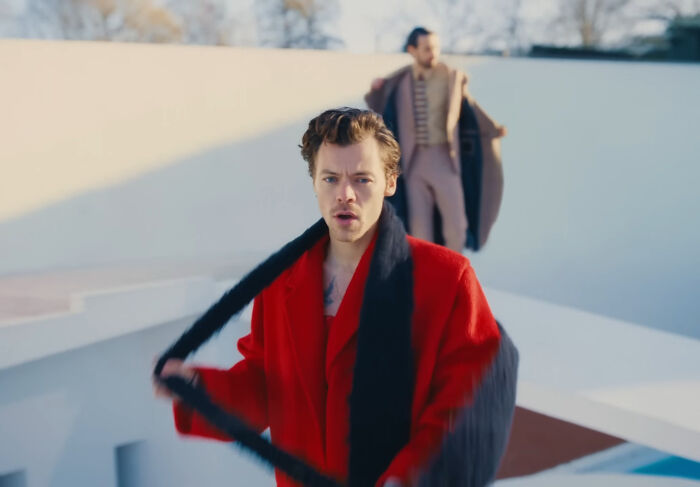 Man in a red coat and black scarf with another man in the background, illustrating moments mere mortals met celebrities.