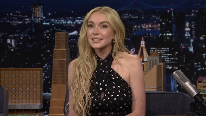 Blonde woman in a black dress sharing a story about encounters with celebrities on a late night talk show set.