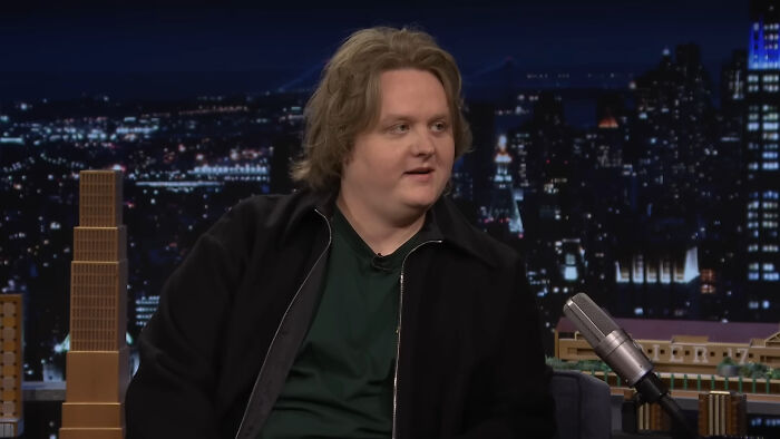 Comedian sitting on a late-night show set, sharing stories about memorable encounters with different celebrities.