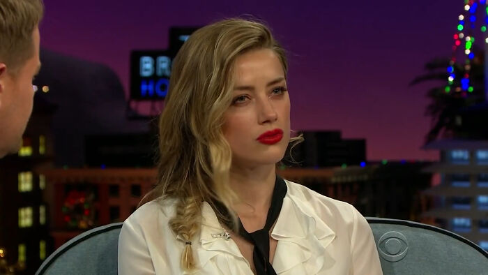 Actress with braided blonde hair and red lipstick during a celebrity interview on a late-night talk show.