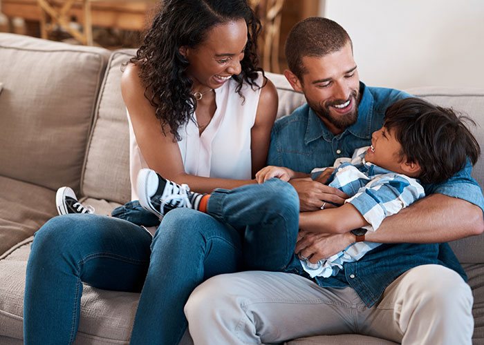 Happy parents playing with their young son on the couch, capturing moments of family and creepy things kids said.
