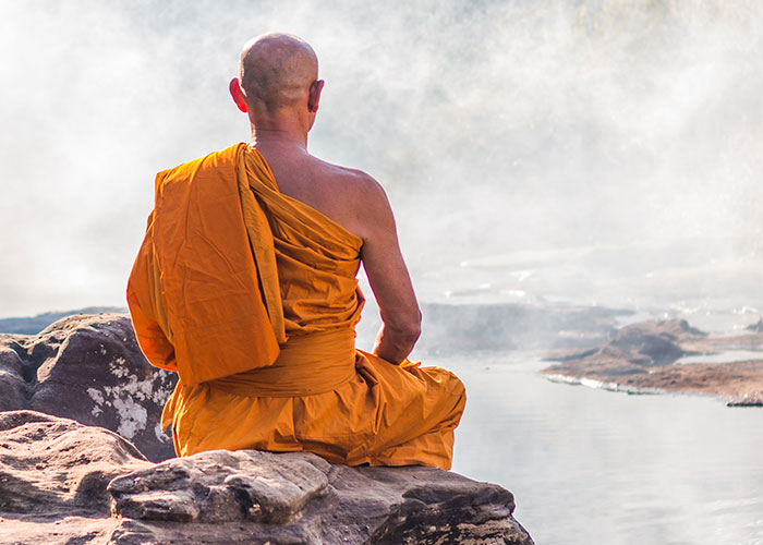 Monk in orange robes meditating on rocks by misty water, evoking a calm yet eerie atmosphere related to creepy kids' sayings.