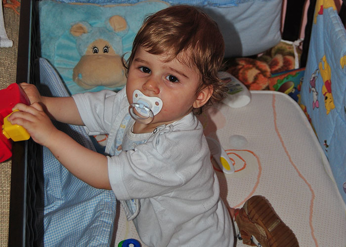 Toddler with pacifier playing in crib surrounded by toys, illustrating creepy things kids said that scared parents.