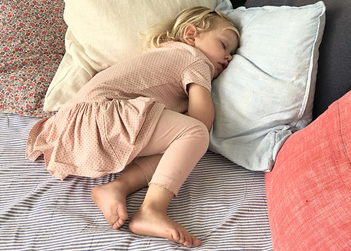 Sleeping toddler curled up on striped bedding surrounded by pillows, captured for creepy things kids said content.