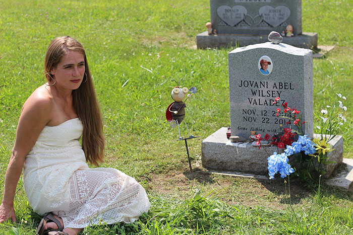 Woman in a white dress sitting by a grave with flowers, relating to Cinnabon worker's daughter and racist tirade story. Woman in a white dress sitting by a grave with flowers, relating to Cinnabon worker's daughter and racist tirade story.