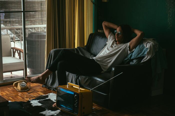 Person relaxing on sofa in dim room with vintage radio and phone, illustrating harmless but toxic habits concept.