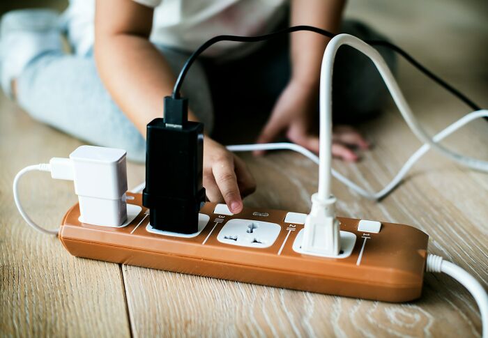 Child discovering a glitch in the system by plugging multiple chargers into a power strip on a wooden floor.