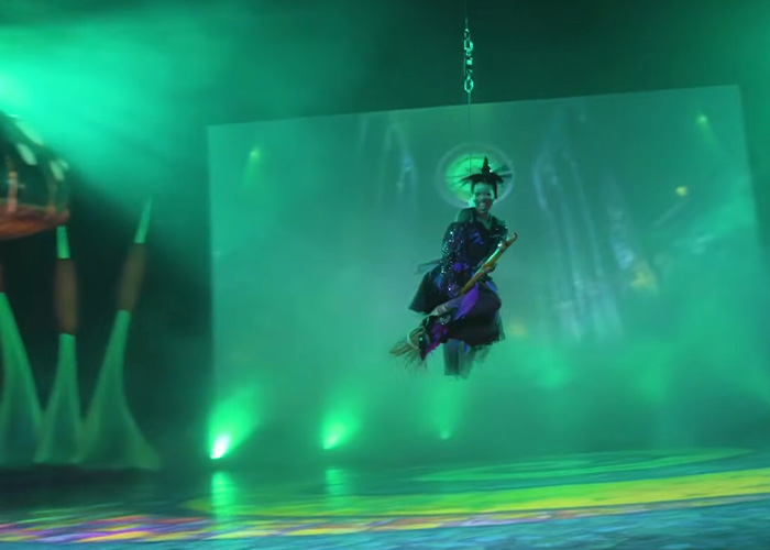 Actor dressed as a witch flying on a broomstick during Wizard Of Oz performance with dramatic green stage lighting and fog effects. Actor dressed as a witch flying on a broomstick during Wizard Of Oz performance with dramatic green stage lighting and fog effects.