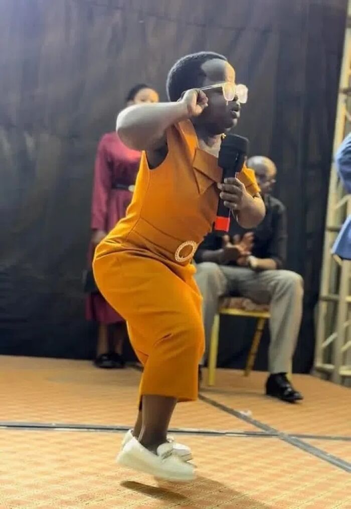 Person in orange dress dancing on stage holding microphone, a moment that made them an internet icon and viral sensation.