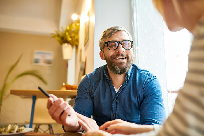Man in glasses and blue shirt discussing craft skills frustration with another person in a bright, casual setting.