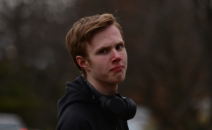 Young man upset outdoors, wearing black hoodie and headphones, expressing frustration over craft skills and family business.