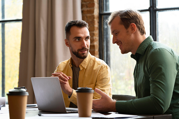 Two men collaborating at a table with laptops and coffee, symbolizing craft skills and business partnership.