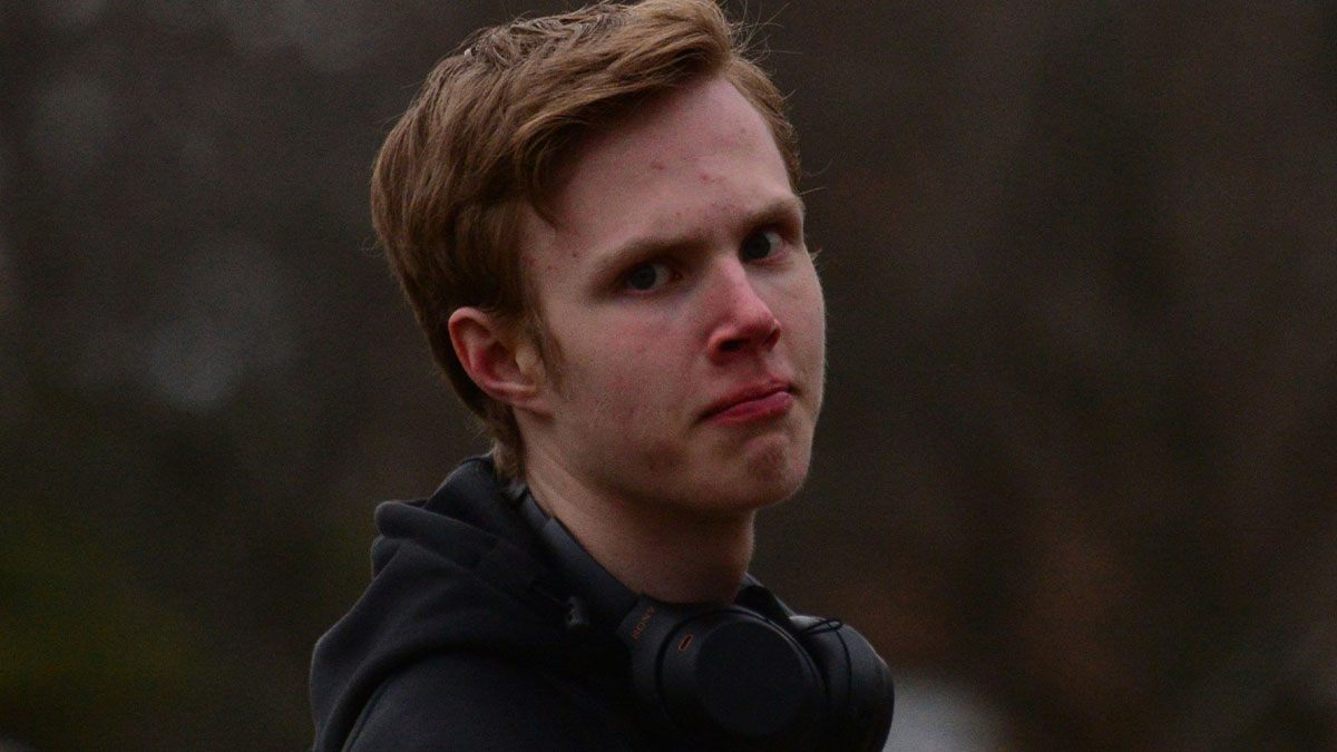 Young man looking upset outdoors, wearing black hoodie and headphones, reflecting on craft skills and family business conflict