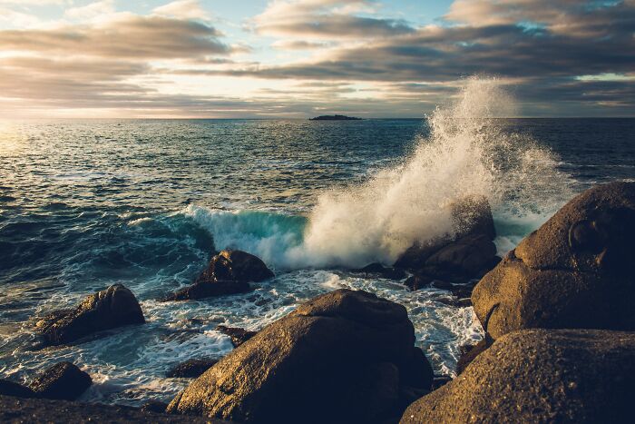Waves crashing against rocks at sunset, illustrating nature’s power and beauty in chaotic motion by the ocean shore.