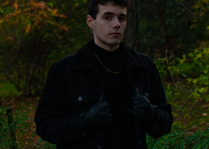 Young man wearing black jacket and gloves standing outdoors in a forest, illustrating survival hacks that can be dangerous.