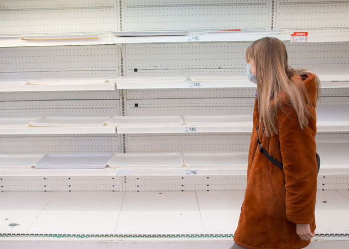 Woman in brown coat looking at empty shelves in store, illustrating survival hacks that can be useless or dangerous.