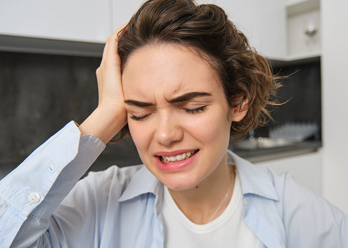 Young woman in casual clothes looking stressed and in pain, highlighting dangers of survival hacks that can be harmful.