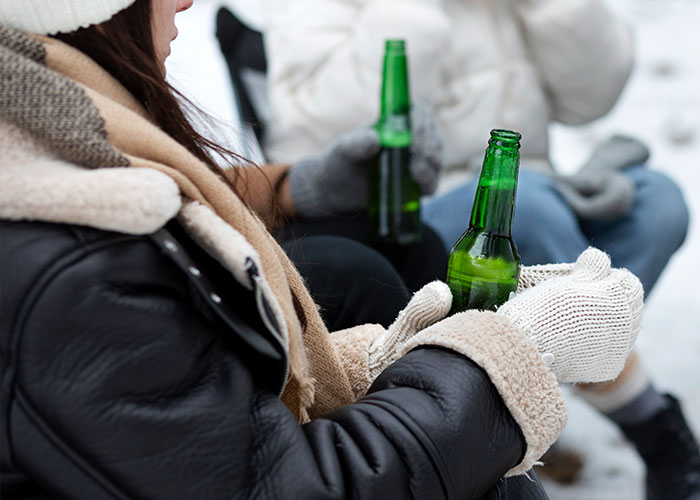 Person wearing warm gloves and jacket holding green bottle outdoors, illustrating survival hacks that can be dangerous.