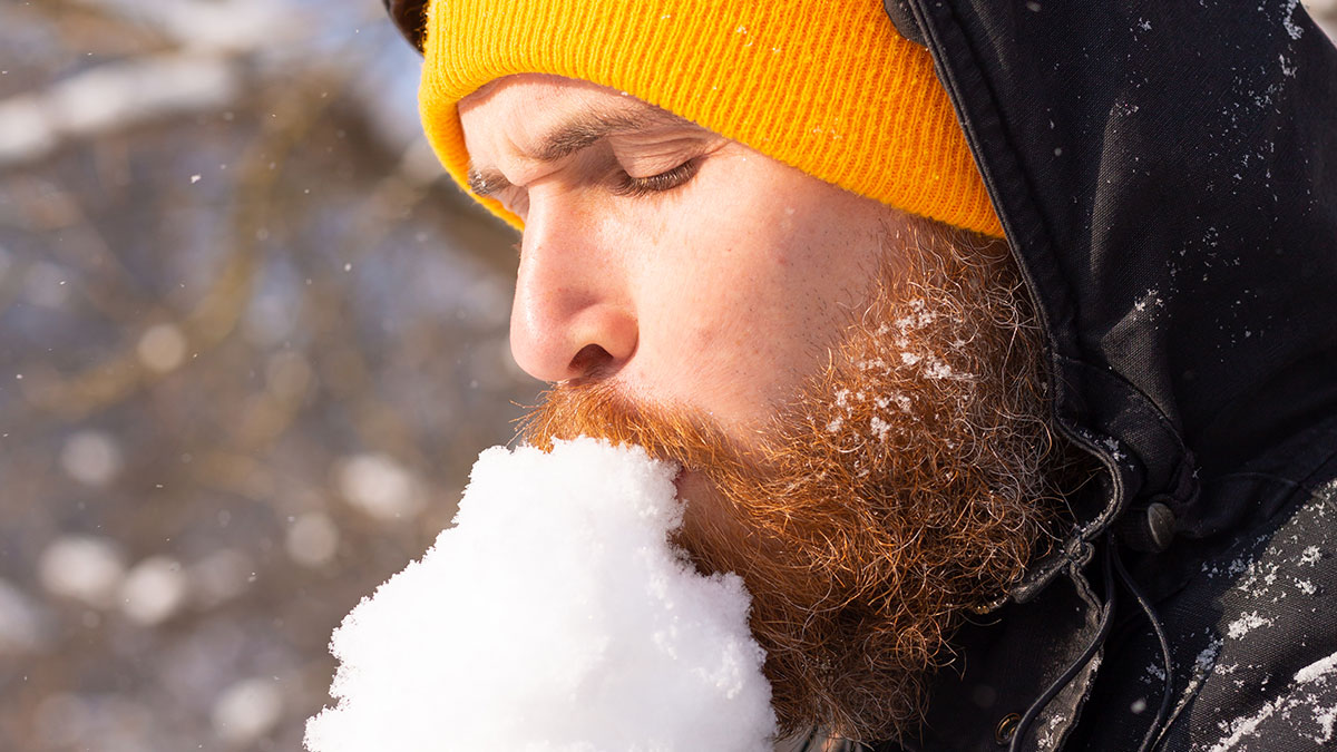 Man with a beard in a yellow beanie biting snow illustrating dangerous survival hacks in cold environments.