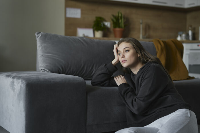 Young woman in casual clothes sitting by a couch, reflecting on experiences with dating outside of their culture.