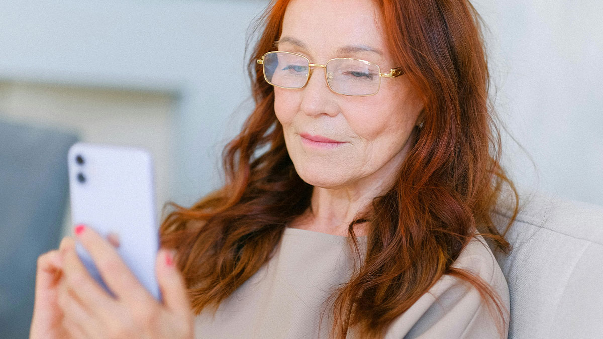 Woman with red hair and glasses looking at phone, reflecting on gay daughter not coming home for Christmas over past joke