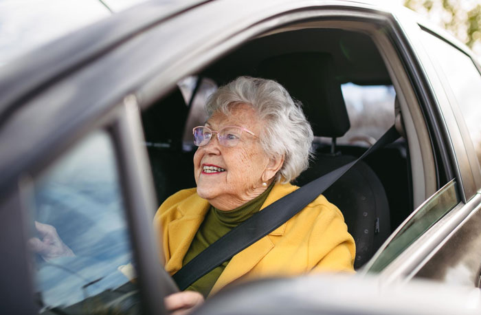 Elderly woman with white hair smiling inside a car, wearing a yellow jacket and seatbelt, enjoying the ride. Elderly woman with white hair smiling inside a car, wearing a yellow jacket and seatbelt, enjoying the ride.