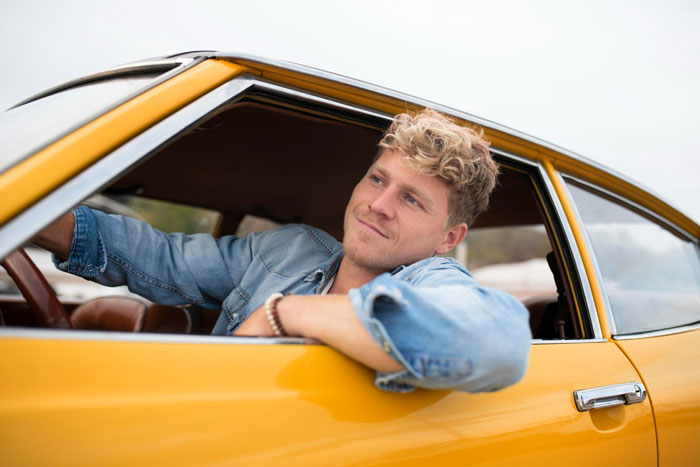 Teen sitting in a yellow car, looking content while leaning out the driver’s side window on a clear day. Teen sitting in a yellow car, looking content while leaning out the driver’s side window on a clear day.