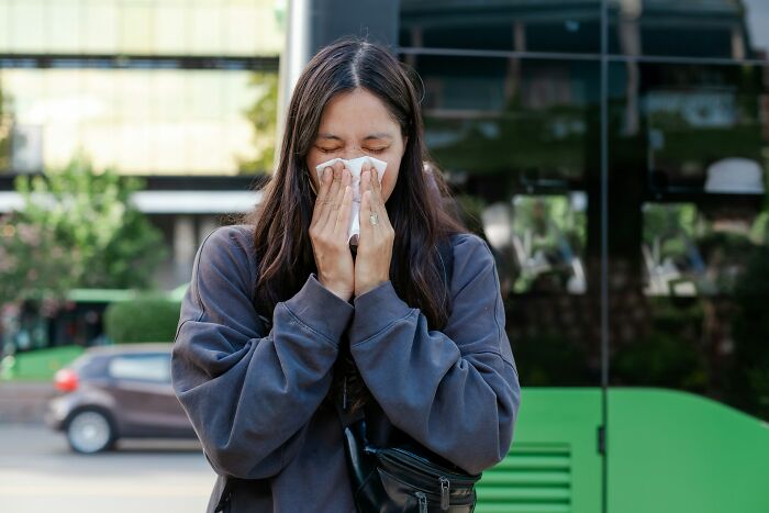 Young woman in casual clothes sneezing into a tissue outdoors, depicting a moment of frustration and entitlement.