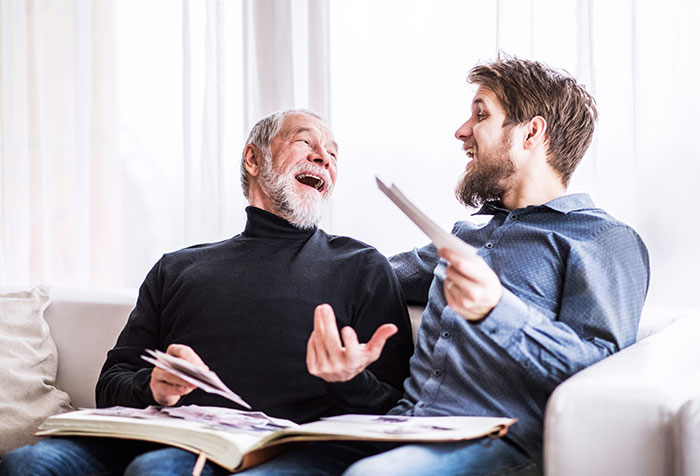 Two men laughing and looking at photos together, illustrating disturbing things found in homes of seemingly normal people.