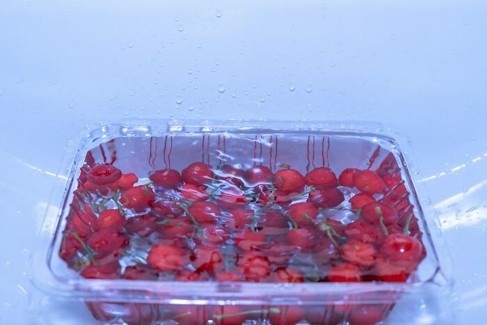Plastic container filled with small red cherries submerged in water, illustrating small design mistakes and cluttered packaging.