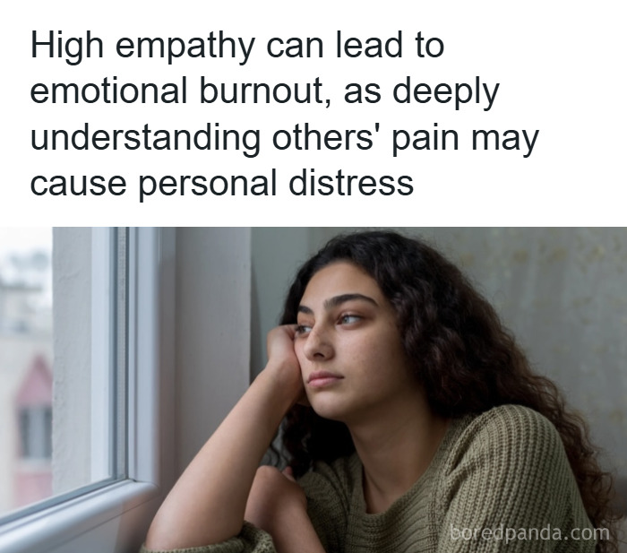 Young woman with curly hair wearing a green sweater looking pensive by a window, illustrating psychology facts on empathy.