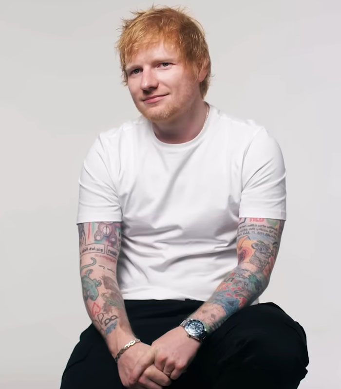 Ed Sheeran sitting with visible tattoos wearing a white t-shirt, spotlighting his shredded physique for Men's Health cover debate.