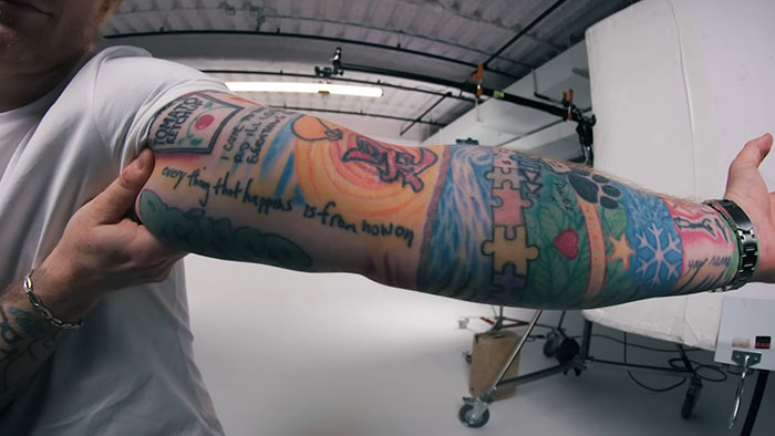 Close-up of a tattooed arm in a studio setting, highlighting detailed colorful designs and script text.