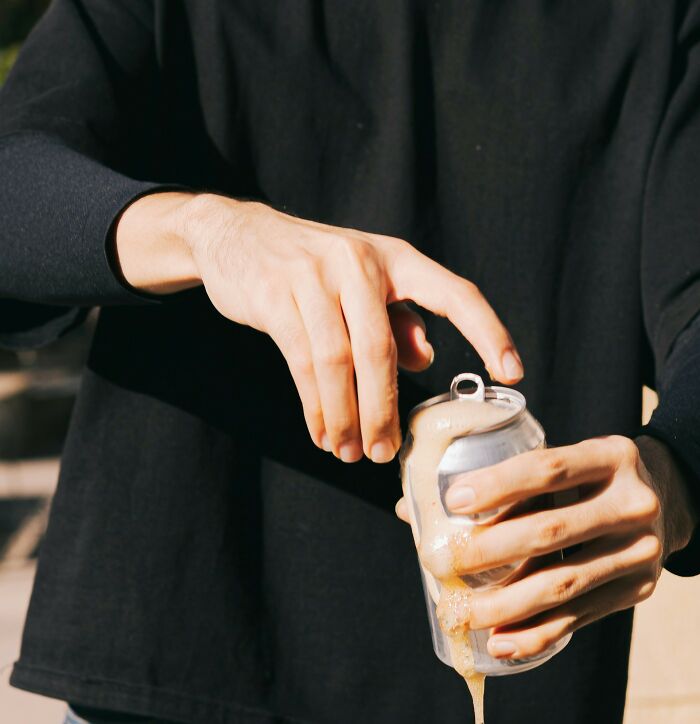 Person in black shirt opening a foaming soda can, illustrating unexpected moments at funerals not going as expected.
