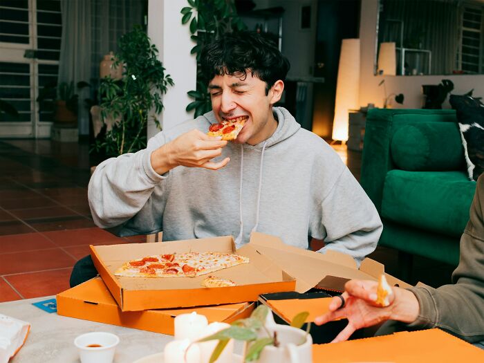 Young man enjoying pizza at home, capturing a moment of a glitch in the system food hack with friends.