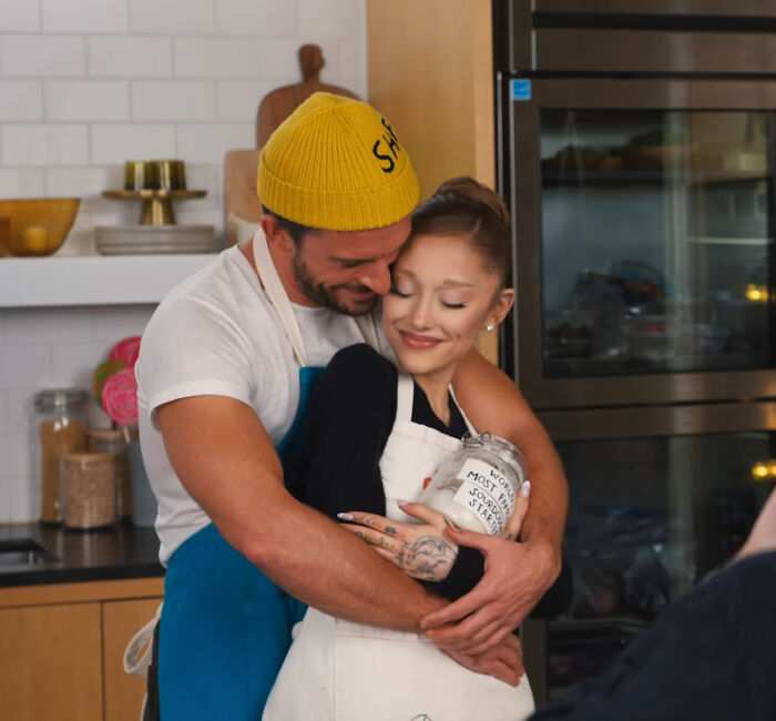 Ariana Grande with a man in a kitchen, sharing a warm embrace amid discussions of her struggles and family support. Ariana Grande with a man in a kitchen, sharing a warm embrace amid discussions of her struggles and family support.