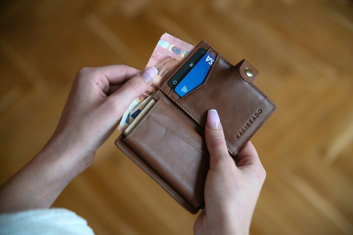 Person holding a brown leather wallet with cash and cards, illustrating unusual personal belongings lost and found items.