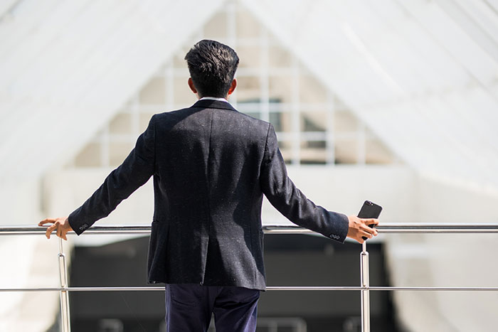 Man in a suit holding a phone, standing alone and looking ahead, symbolizing boss and employee conflict leading to firing.
